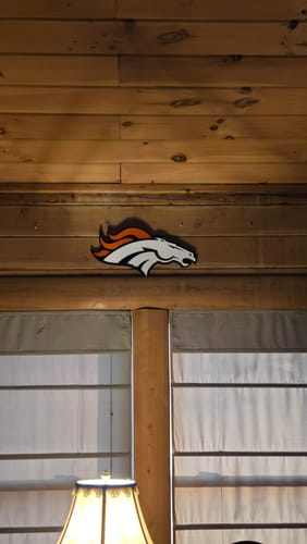 Reviewer's Denver Broncos 3D metal wall art mounted on a rustic, wood-paneled wall in their home.