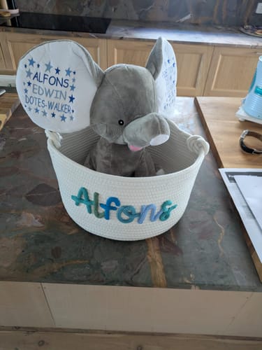 Customer's white knitted basket personalized with the name 'Alfons' in multicolor yarn, with a stuffed elephant sitting inside.