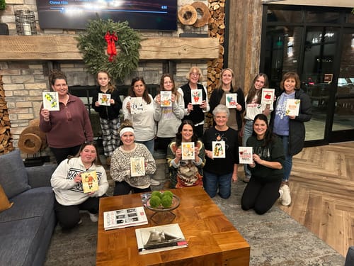 A large group of reviewers holding up their completed mini paintings from the Christmas paint-by-number set.
