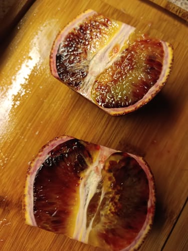 Ein Kunde zeigt zwei Hälften einer saftigen, tiefroten Moro Blutorange auf einem Holzbrett.