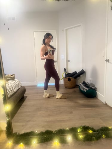 Customer taking a mirror selfie in a bedroom, showing a side profile of the dark red The V Legging set.