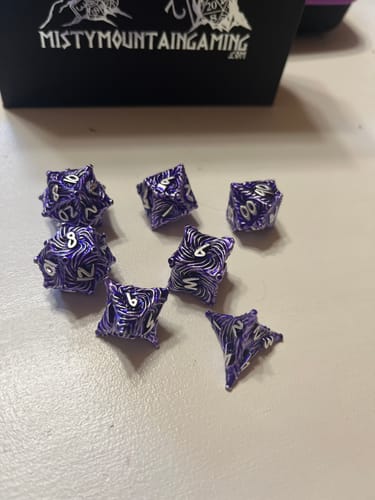 Customer's purple Vortex Warp Metal Dice Set with a mesmerizing swirl pattern scattered on a light surface.