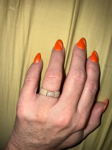 A reviewer's hand with bright orange nails wearing the light-colored silicone ring with a rectangular stone setting.
