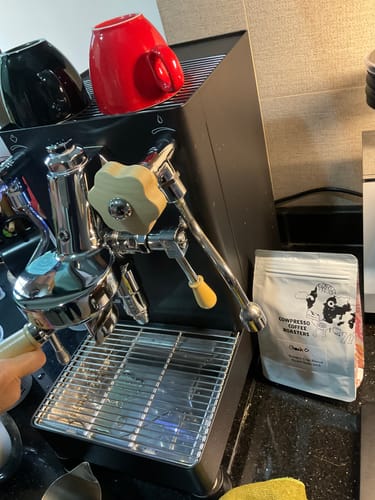 Customer's bag of Golden Cup Blend coffee on a counter next to a black and chrome espresso machine.