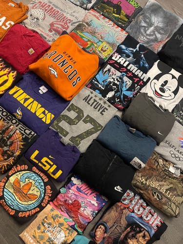 Customer's haul from the Trendy Mix Bale spread out, showing assorted graphic tees and sweatshirts with sports and character logos.
