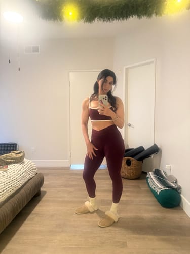 Customer taking a mirror selfie in a bedroom, showing a front-angled view of the dark red The V Legging set.