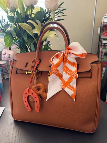 Customer's brown LALUVA Warkin Leather Bag on a table, styled with a decorative scarf and charm.