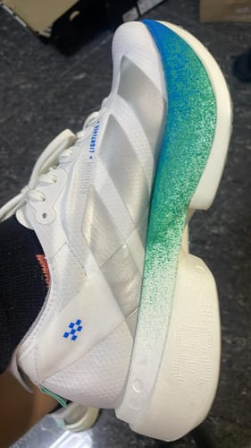 Customer's side view of the white Adizero Adios Pro 4 shoe, showing the thick sole with a blue and green gradient.