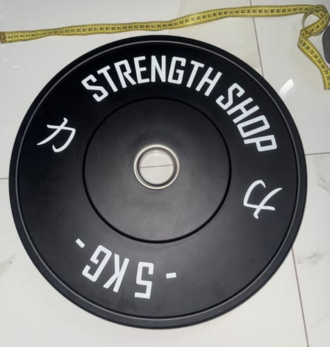 Customer's black 5kg Rubber Bumper Plate on a tiled floor, shown with a measuring tape.