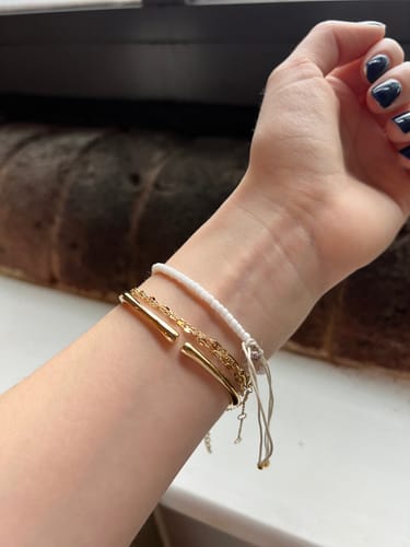 Close-up on a reviewer's wrist showing the open, adjustable ends of the gold Bamboo Bangle.