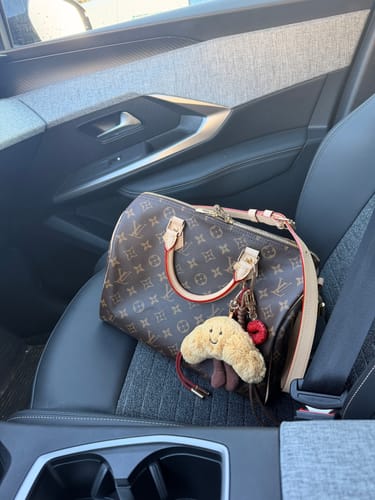 Customer's KISS-ME CROISSANT GIRL STACK CHARM attached to a brown handbag on a car seat.
