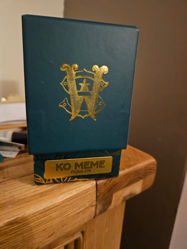 Reviewer's dark teal and gold packaging for Ko Meme perfume sitting on a wooden table.