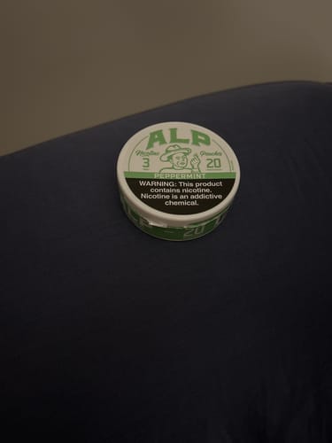 Customer's can of ALP Peppermint Nicotine Pouches with its green and white label on a dark surface.