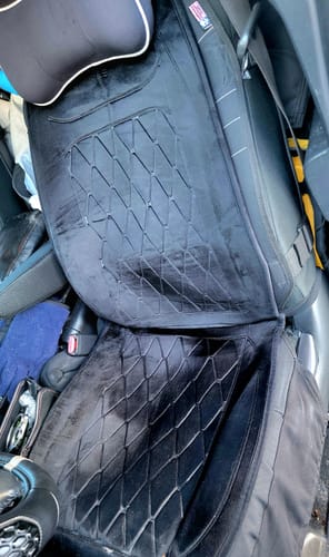 Rezensent zeigt den schwarzen, gesteppten beheizten Autositzbezug auf einem Autositz.