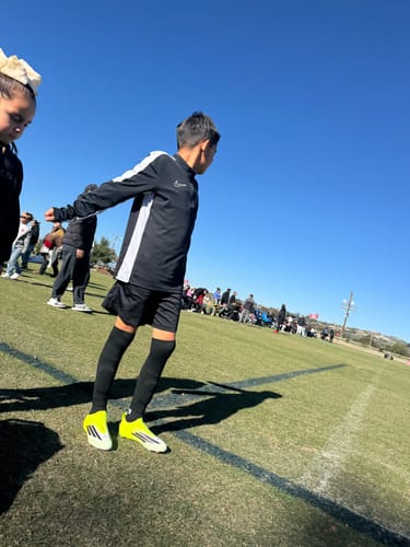 Customer's son wearing the black Built-In Shin Pad sleeves on a sunny soccer field.