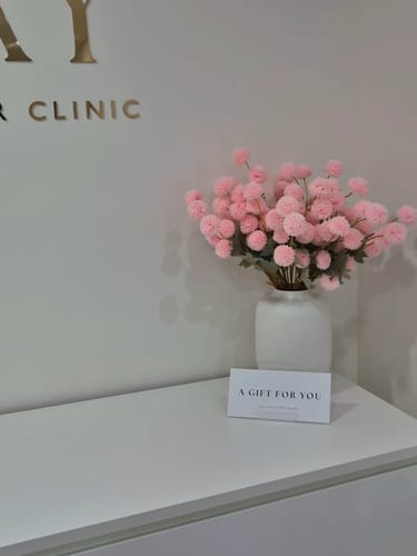 Recensent toont het volle boeket roze Kiku bloemen in een witte vaas op een toonbank.
