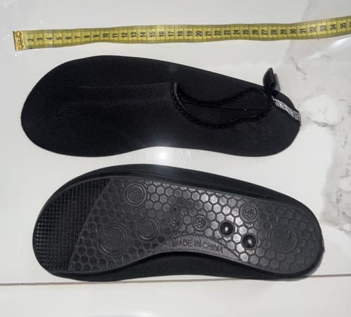 Reviewer's black Riot Deadlift Slippers. One shows the top, the other shows the textured sole, with a measuring tape above.