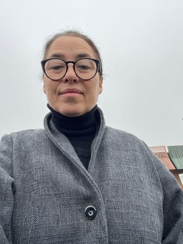 Cliente portant la Veste Faustine grise et texturée par-dessus un col roulé.