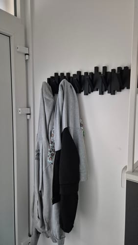 Recensent toont de zwarte Umbra Sticks wandkapstok in gebruik achter een witte deur.