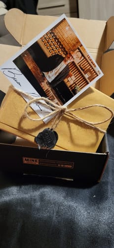 Cliente mostra la confezione del profumo ARCHÉ all'interno della scatola, elegantemente legata con uno spago e un sigillo di cera.