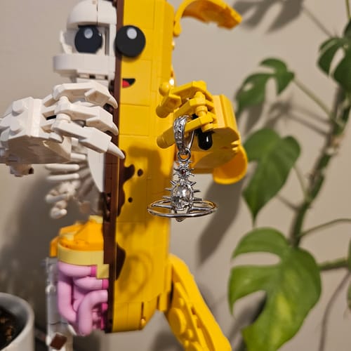 Customer's silver ORBITUARY PENDANT held by a yellow and white toy figure, showing its detailed skull and spikes.