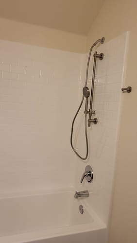 Customer's installed Slide Bar with Handheld Shower Head Set on a white acrylic shower wall over a bathtub.