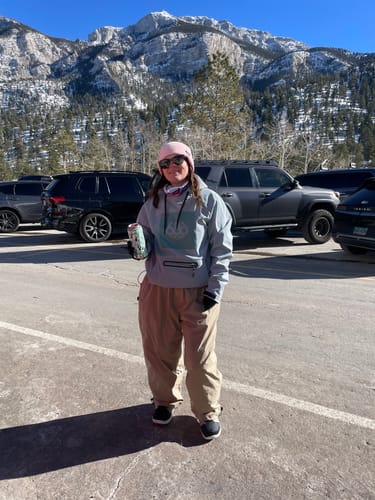 Reviewer showing the baggy fit of the khaki Snow Pants in a mountain parking lot.