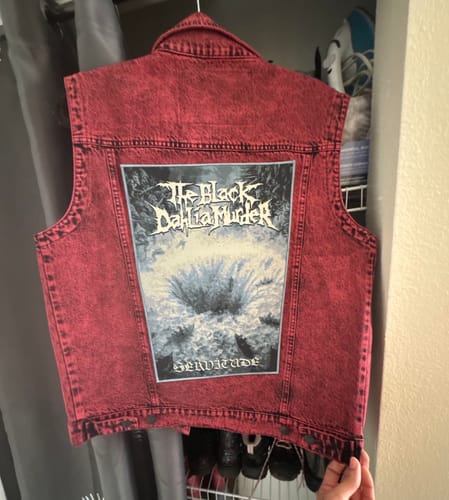 Reviewer showing a large band patch sewn onto the back of a red acid-wash denim vest.