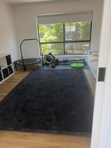 Customer's large, dark grey Mellow Mat in a playroom with exercise equipment in the background.
