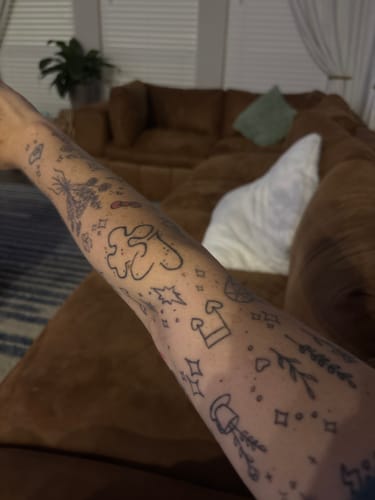 Reviewer's arm covered in a variety of small, simple line-art tattoos.