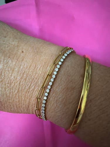 Close-up of a reviewer's wrist, showing the layered gold Luna Bracelet Bundle against a bright pink background.
