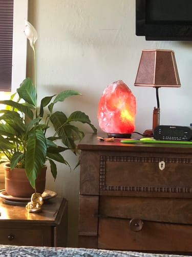 Customer's lit Himalayan Salt Lamp glowing warmly on a wooden dresser next to a houseplant.