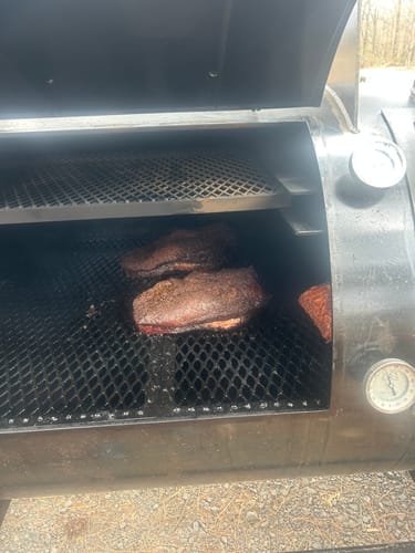 Customer's two USDA Prime Briskets with a dark bark smoking on the grate of a large smoker.