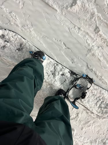 Reviewer's view looking down at their baggy dark snow pants while standing on a snowboard.
