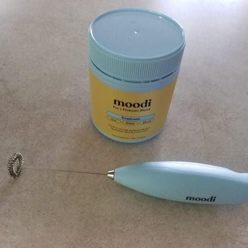 Customer's tub of Tropicana Pre + Probiotic Blend and matching light blue frother on a countertop.