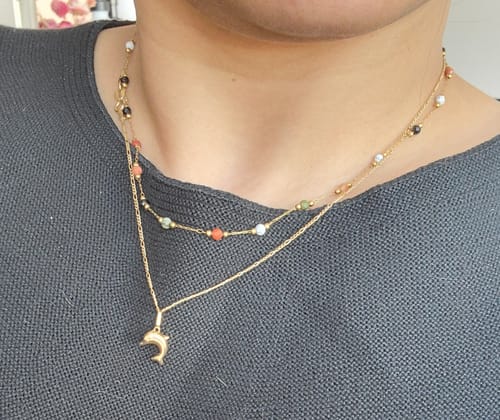 Reviewer wearing the Lulu Beaded Stone Necklace layered with a gold dolphin pendant necklace.