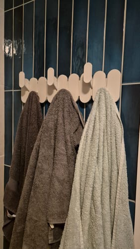 Klant gebruikt de zandkleurige Umbra Tempo wandkapstok voor handdoeken in de badkamer.