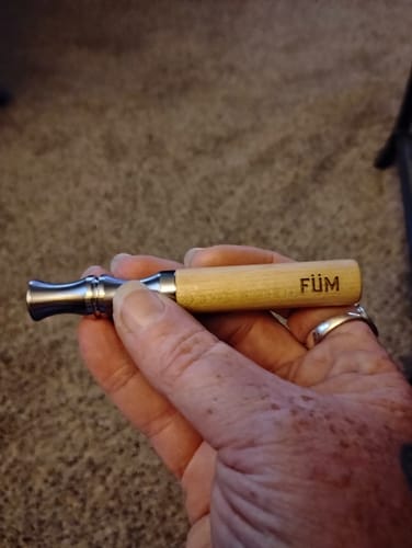 Customer holding the wooden Füm V2 aromatherapy device in their hand against a carpeted background.