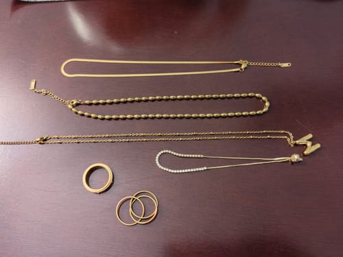 Reviewer's waterproof jewelry bundle, featuring various gold-colored necklaces and rings laid out on a dark surface.