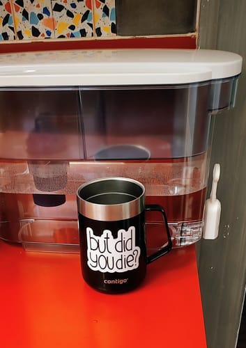 Reviewer's 'But Did You Die? Sarcasm Sticker' on a black travel mug sitting on a red surface.