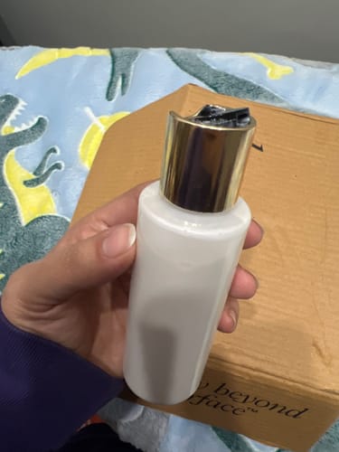 Close-up of the DREAM GLAZE Peptide Milk Toner bottle held in hand, showing the new gold press-top cap.