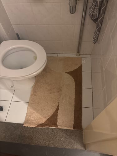 Recensent toont de beige Badmat Bowie met abstract patroon op een witte tegelvloer.