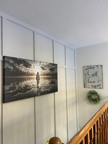Customer's Walking on Water canvas art hanging on a white paneled wall next to a staircase.