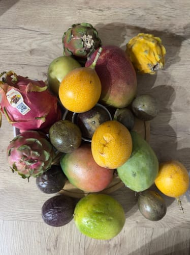Ein Kunde zeigt die frischen Mangos und verschiedenen Drachenfrüchte aus der Duo Box auf einem Holztisch.