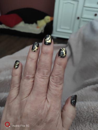 Hand einer Kundin, die die „Deadly Gorgeous“ UV-Gel-Nagelfolien mit schwarzem und goldenem Design trägt.