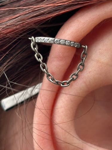 Close-up of a reviewer wearing the chained clicker earring in a cartilage piercing, showing the gem-paved hoop and short chain.