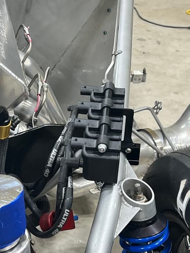 Customer's close-up view of the black Rollbar Mount Coil Brackets holding ignition coils on a silver vehicle rollbar.