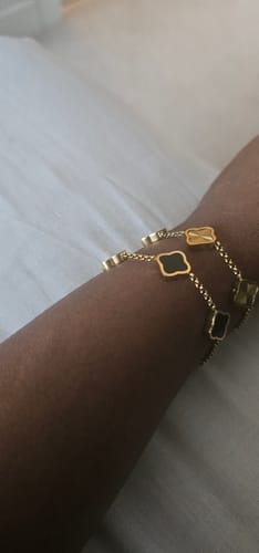 Close-up of a customer's wrist wearing two stacked Celine Clover Bracelets with black and gold motifs.