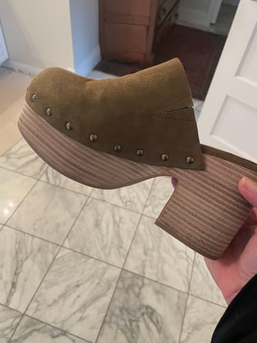 Reviewer holding up an olive suede GIGI platform clog, showing the faux wood heel and stud details.