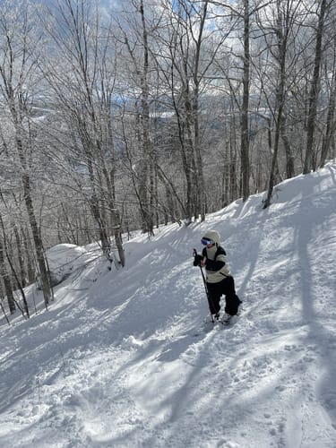 Reviewer skiing on a snowy, tree-lined slope wearing the black Baggy Snow Pants.